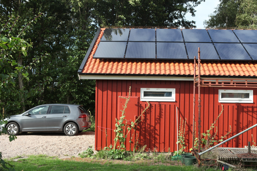 Elbil bredvid ett garage med solceller på taket.